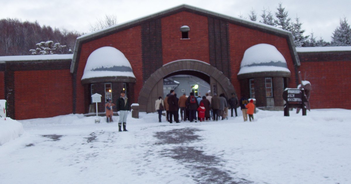 雪地裡的博物館網走監獄紅磚正門:兩側圓頂小屋頂上積著雪,一群穿冬衣的遊客正走進中央的拱門