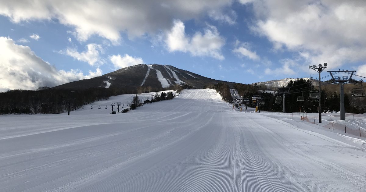 安比高原滑雪場的白樺ゲレンデ,剛壓好的寬闊雪道一路延伸到前森山腳下,山坡上有幾條白色雪道,右側是吊椅支柱與纜線,雪道上沒有人