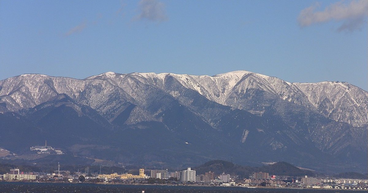 冬天隔著琵琶湖望向比良山系：山頂稜線積著雪，山腳是湖岸的市街，前景是深藍色的湖面