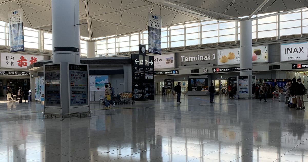 中部機場 Access Plaza 2 樓的大廳:正前方黑色指標寫著左邊往第 2 航廈「T2」、右邊往第 1 航廈「T1」,後方牆上是「Terminal 1」字樣與國內線出發指標,左邊是航空公司航廈對照的告示柱