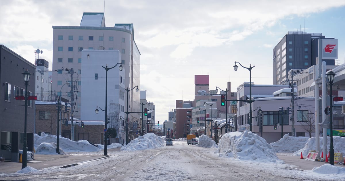 A downtown street in Aomori in January, the asphalt packed with compressed snow and cleared snow banked up along the pavement