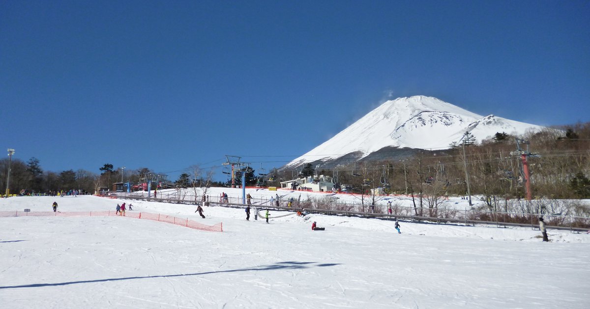 富士山 Yeti 滑雪場山腳平緩的雪坡，晴天藍空，右後方是整座積雪的富士山，中間幾座吊椅支柱與纜線往山上延伸，雪坡上有零星滑雪的人；2015 年 2 月雪季中段拍攝，當時名稱是スノータウン Yeti