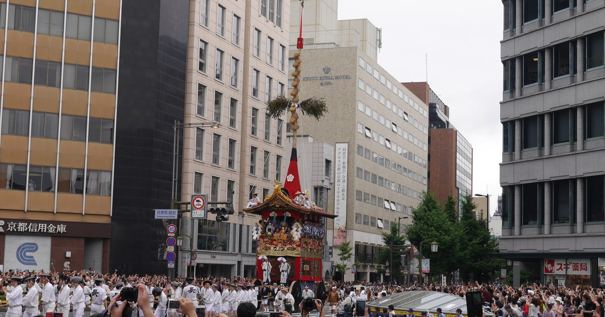 A Gion Matsuri hoko float topped by a tall pine mast moves along Kawaramachi Street in Kyoto as spectators hold phones overhead