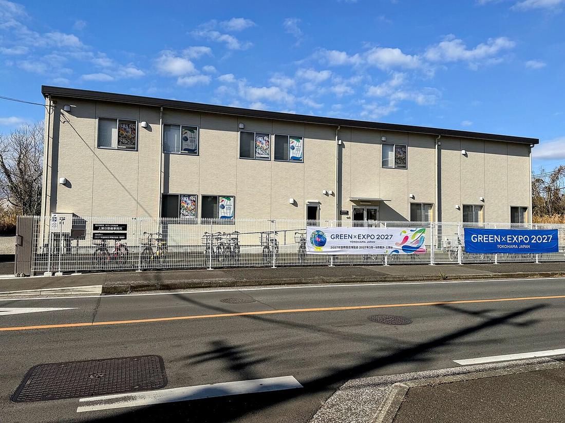 Two official GREEN×EXPO 2027 banners on the fence of the Kamiseya site office in Yokohama, the white one giving the dates as March to September 2027