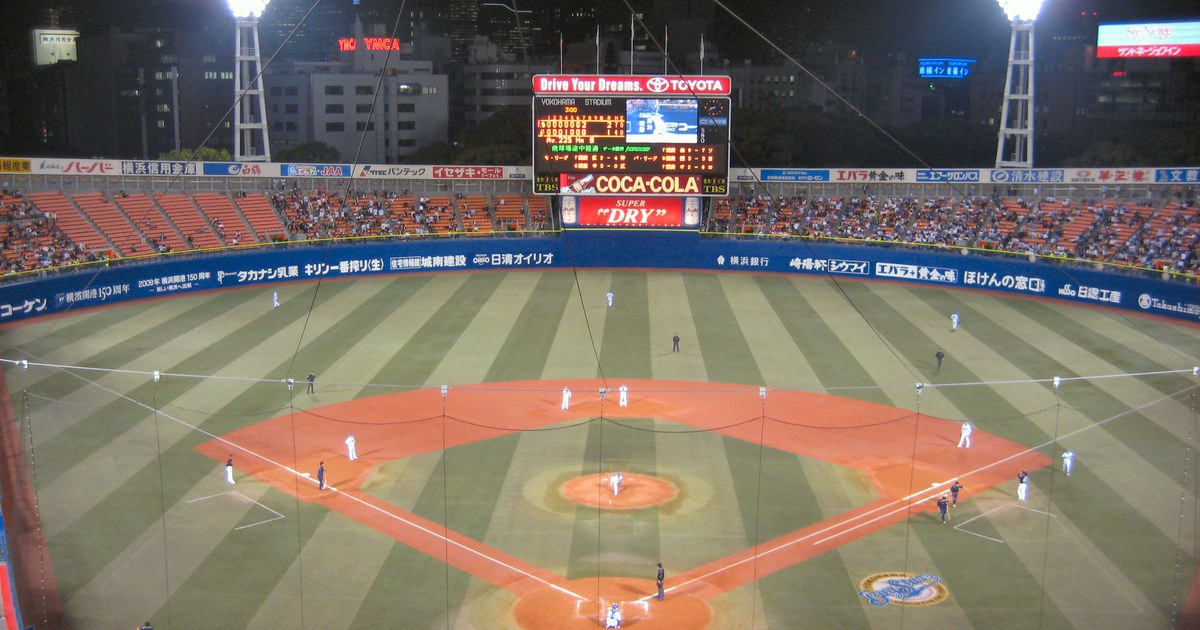 lit by floodlights, spectators in the stands and the scoreboard glowing beyond the outfield
