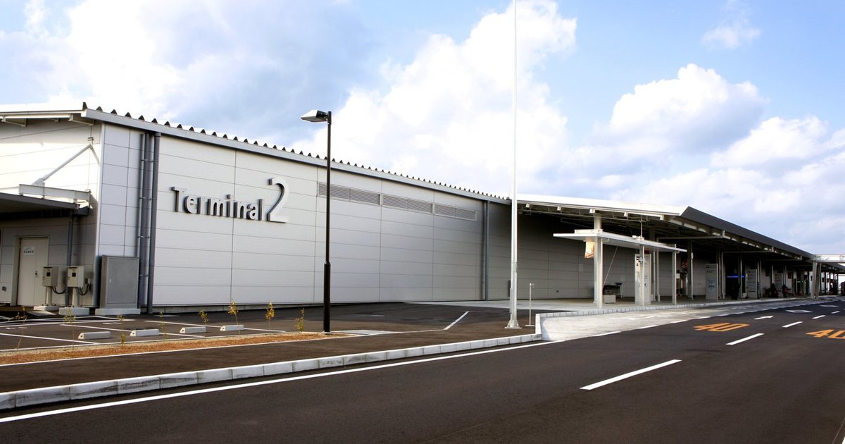 關西機場第 2 航廈外觀：低矮的銀灰色倉庫型建築，外牆寫著「Terminal 2」，門前是車道與有頂棚的上下車處
