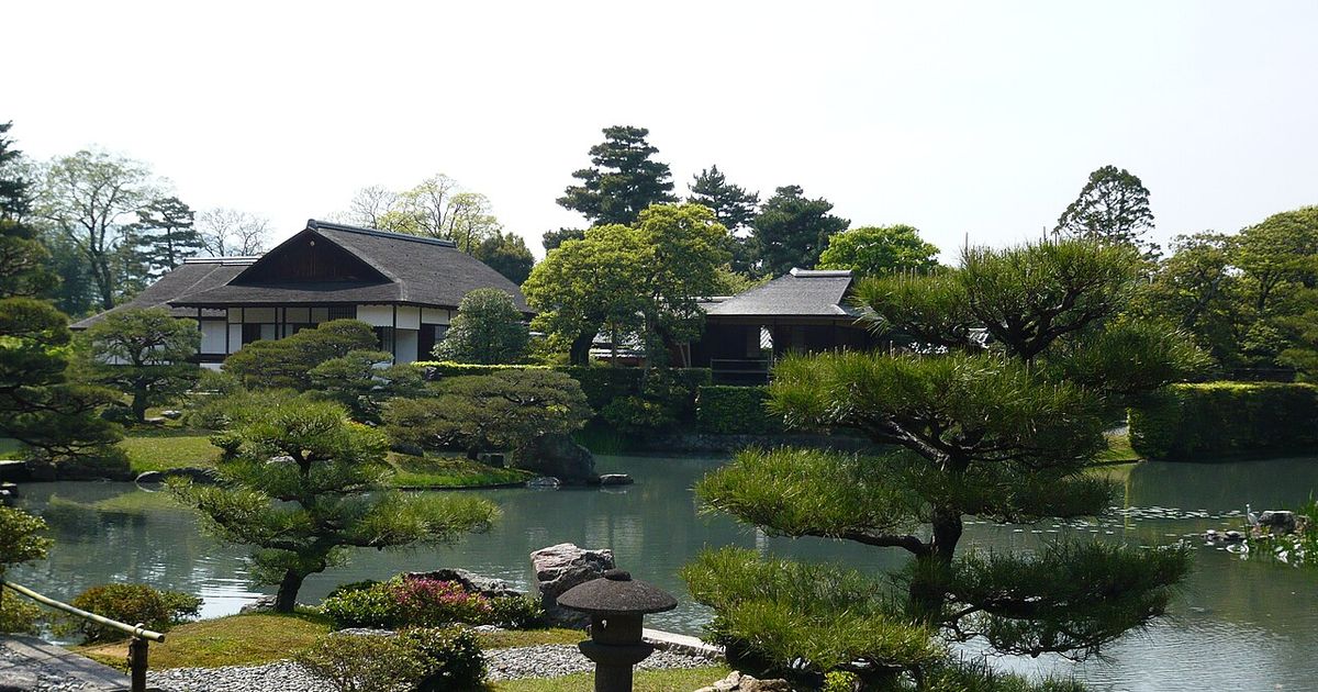 桂離宮的池泉庭園：前景是修剪過的松樹與石燈籠，隔著池水看得到對岸書院一帶的茅葺與瓦屋頂建築