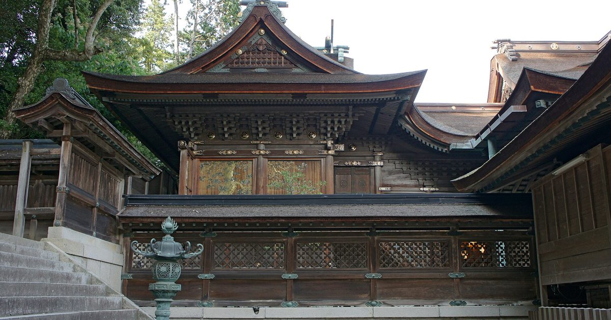 The honden (main sanctuary) of Kotohira-gu's Gohongu: dark timber, gilded metal fittings and latticework, with stone steps and a bronze lantern at lower left