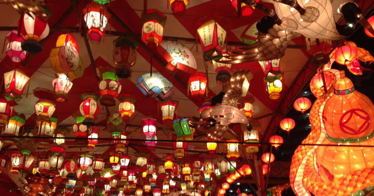 The lantern canopy at the Minato Park venue of the Nagasaki Lantern Festival: hundreds of hand-painted paper lanterns hanging under a red marquee roof, with a giant illuminated gourd-shaped lantern on the right and a white crane-shaped lantern in the centre