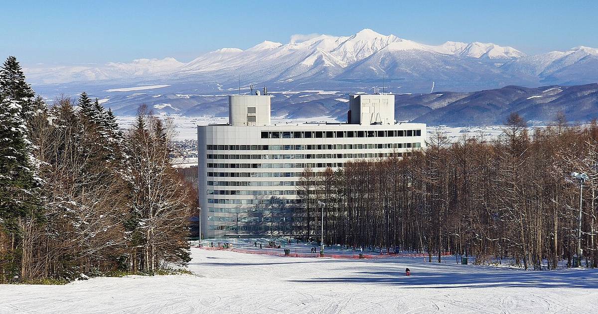 富良野滑雪場富良野區的雪道往下看:雪道盡頭的樹林間立著白色的新富良野王子飯店,後方是積雪的富良野盆地與一整排雪山