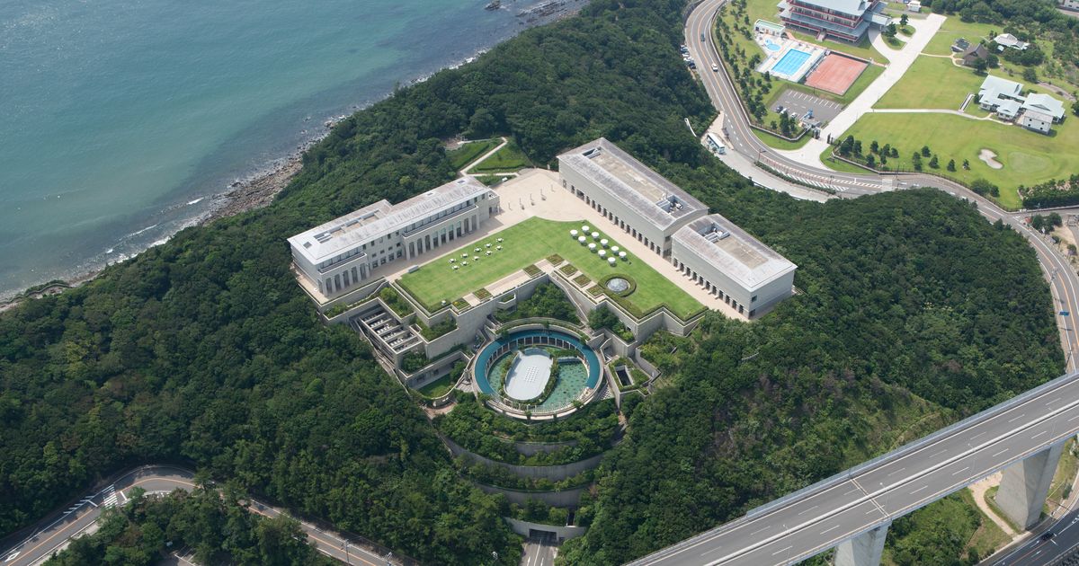 空拍大塚國際美術館:海邊森林小山頭上的白色建築群圍著方形草坪庭園,往下一層是圓形的戶外展區,右下角是往大鳴門橋的高架道路