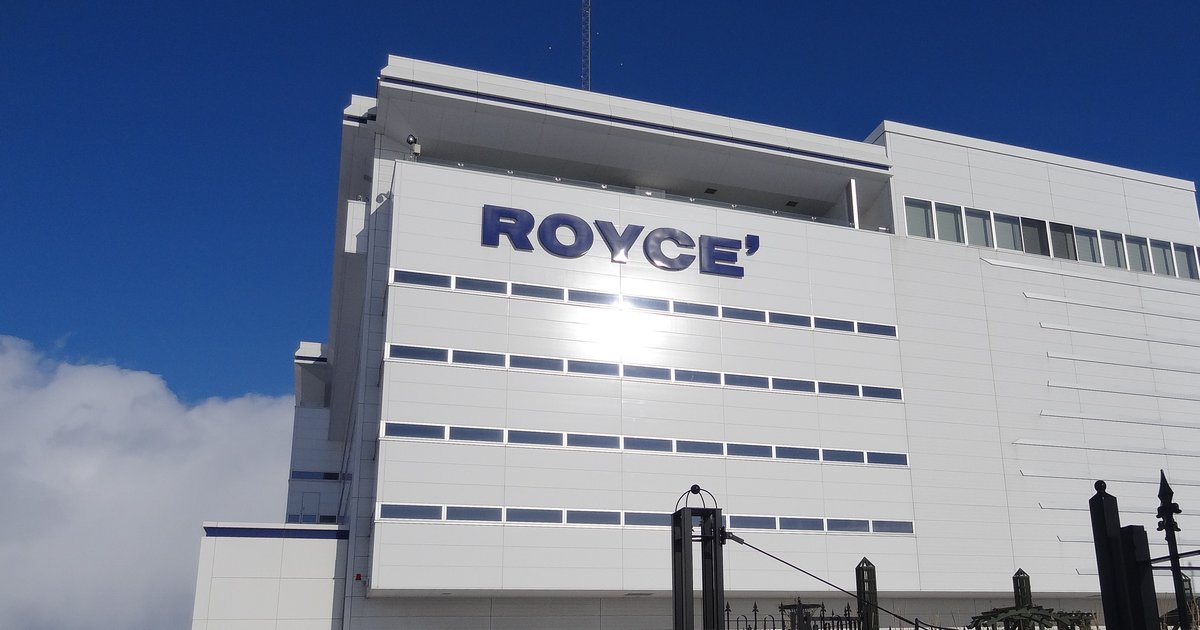 ROYCE' CACAO & CHOCOLATE TOWN 的白色館舍外觀，外牆上方掛著藍色 ROYCE' 字樣，背後是冬天的藍天