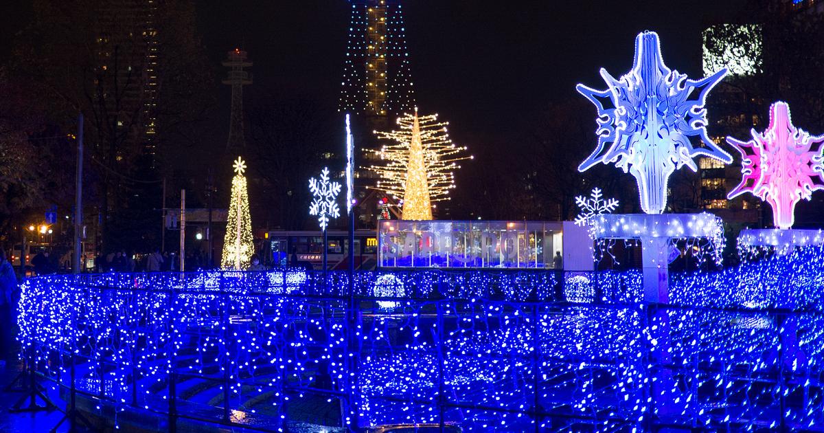 Sapporo White Illumination at Odori Park in November 2016: a railing covered in blue LEDs in the foreground, white and pink snow-crystal light sculptures on the right, a gold tree-shaped light and the Sapporo TV Tower behind
