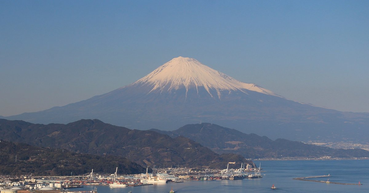 晴朗冬日從日本平往東北看:山頂積雪的富士山聳在深藍色山稜後方,山腳下是清水港的碼頭、貨櫃起重機與市街
