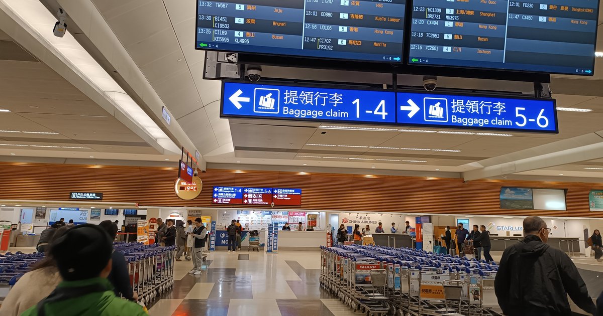 Baggage claim hall at Taoyuan International Airport, with baggage claim signage, arrival boards listing flights from Japan and rows of luggage trolleys