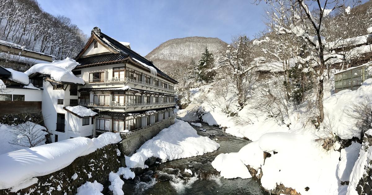 寶川溫泉汪泉閣的冬天：晴天的積雪溪谷裡，多層的和風旅館建物沿著寶川的石砌河岸蓋起，屋頂與兩岸堆滿厚雪