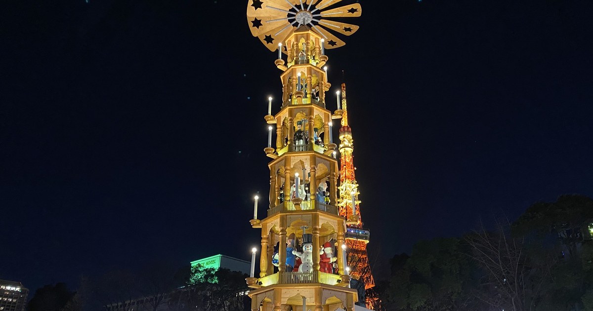 2019 年 12 月東京聖誕市集芝公園會場的夜景:打著暖黃燈的多層木造聖誕金字塔,各層站著木偶、外圈一圈燭形燈,右後方是亮橘色燈的東京鐵塔