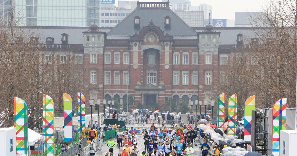 東京馬拉松終點前的行幸通:紅磚的東京站丸之內站舍正對著賽道,兩側立著彩色旗幟,跑者從遠處跑來,雨天