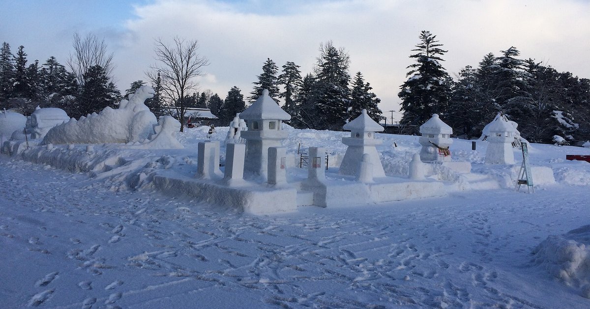 上杉雪燈籠祭會場白天的樣子：雪地上一組用雪堆成、還沒點燈的雪燈籠與雪柱圍成的方陣，後方是覆雪的杉樹林和幾座雪雕，地上滿是腳印