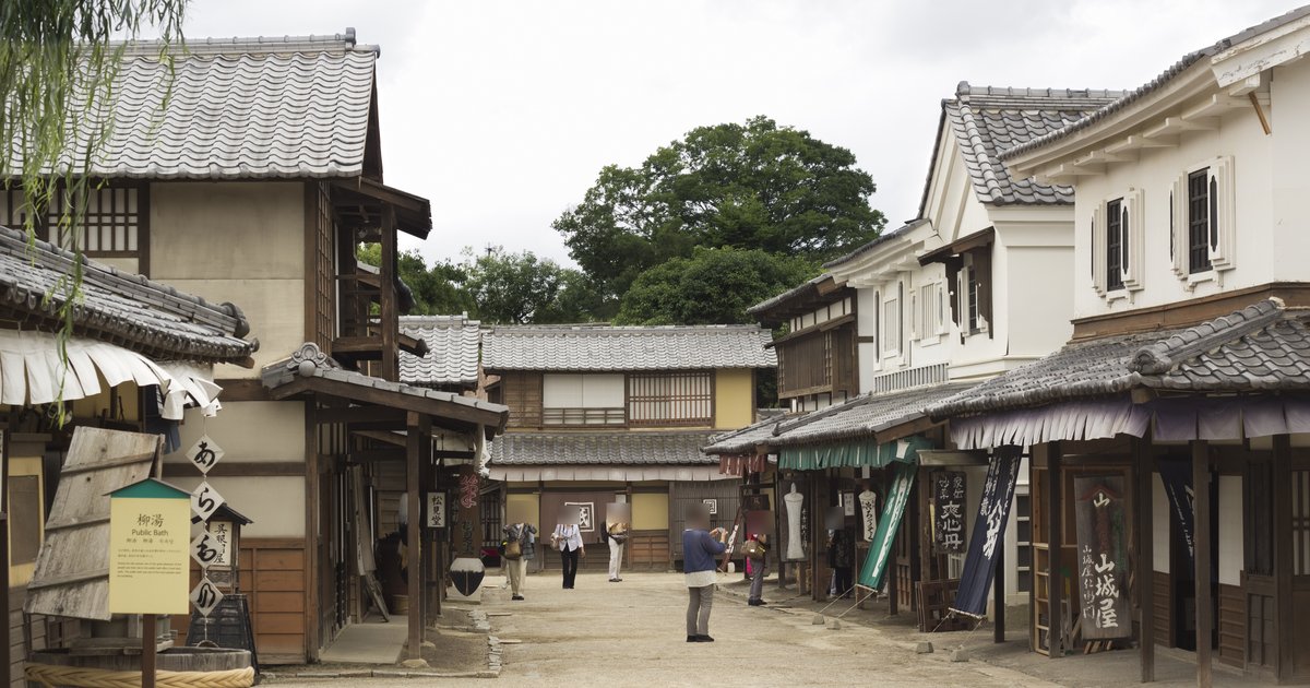 太秦映畫村的江戶街景外景區:碎石路兩側是瓦頂木造町家與白牆商家,掛著「山城屋」等木招牌與深藍布幡,左邊有「柳湯 Public Bath」的解說牌,路中間有幾位遊客在拍照