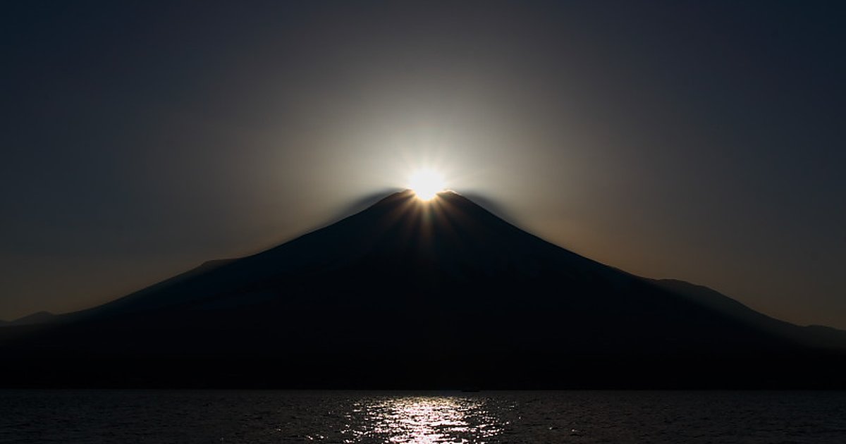 山中湖的鑽石富士：夕陽正好落在富士山頂，山頂迸出一圈放射狀光芒，富士山整座是深色剪影，下方湖面映著一道金色光帶