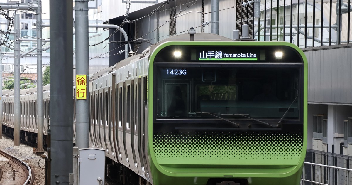 The lime-green front end of a Yamanote Line train approaching, its black destination panel reading 山手線 Yamanote Line, the run number 1423G shown above the windscreen, and a yellow trackside sign in red characters reading 徐行 (proceed slowly) on the left.