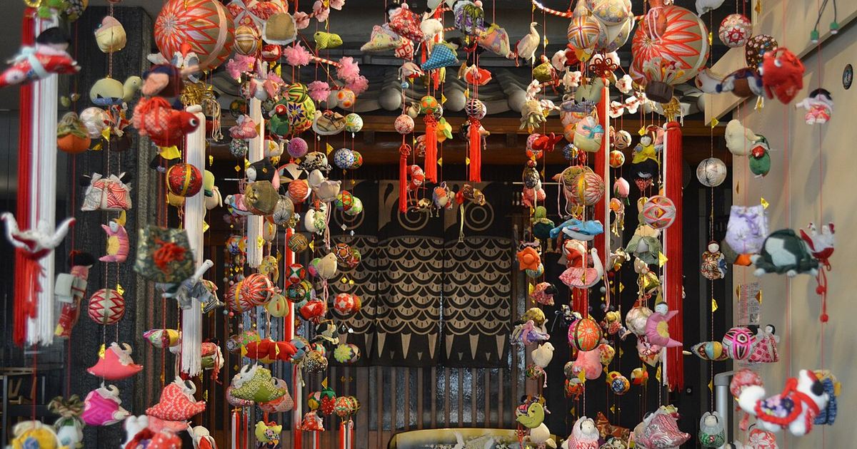 柳川雛祭期間店內掛滿的さげもん:一串串紅線垂下布製的鶴、兔子、金魚等小吊飾與彩色刺繡的柳川鞠,後方是深色暖簾