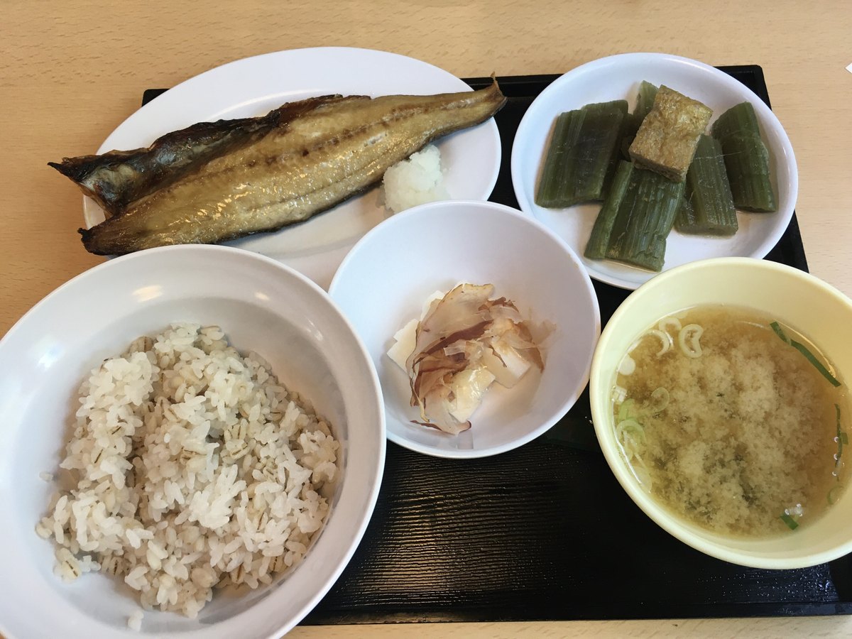黑色托盤上的監獄食:一整片烤花魚配蘿蔔泥、一碗混著麥粒的麥飯、一碗味噌湯、一小碗撒柴魚片的小菜、一盤綠色的燉煮蔬菜