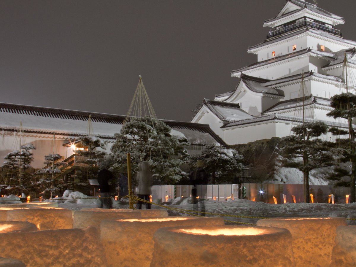 晚上的鶴城：前景是幾座用雪堆成、中間點著燭火的雪燈，後方一排小燭燈，右上是屋頂積雪、打亮的天守閣，中間有兩三個模糊的人影