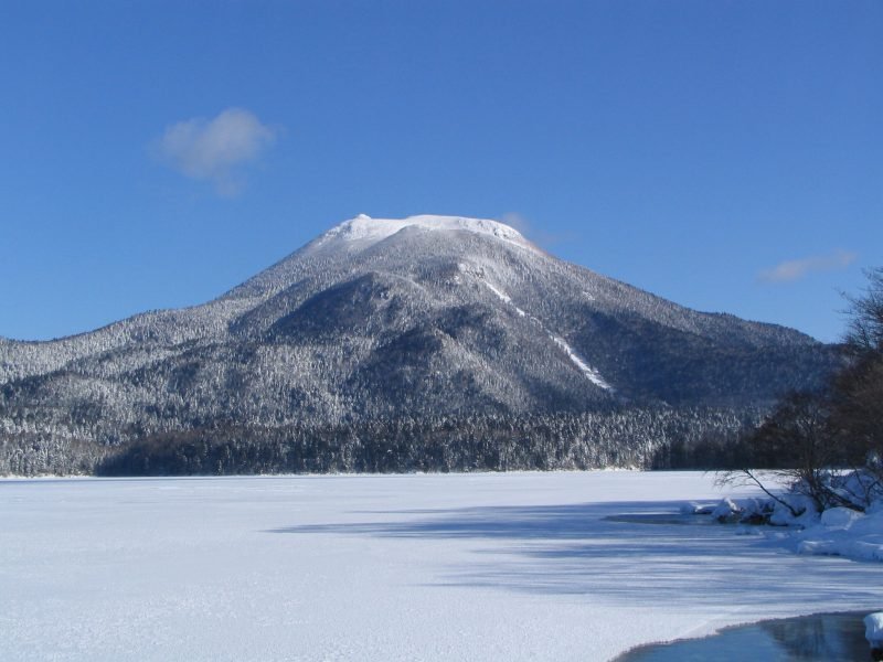1 月的阿寒湖全面結冰,雪白的湖面一路延伸到對岸,後方是整片被雪覆蓋的雄阿寒岳,右下角有一小塊尚未結冰的深色水面