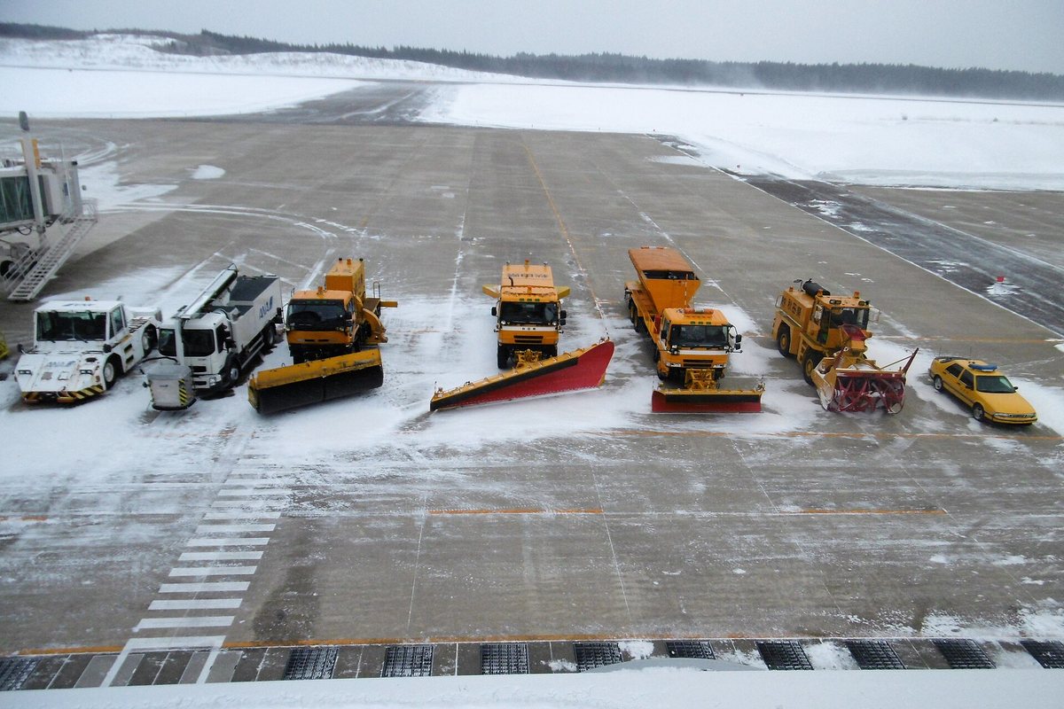 A line of snow-clearing vehicles on standby on the apron at Odate-Noshiro Airport in Akita, including plough trucks, a spreader and a rotary snow blower