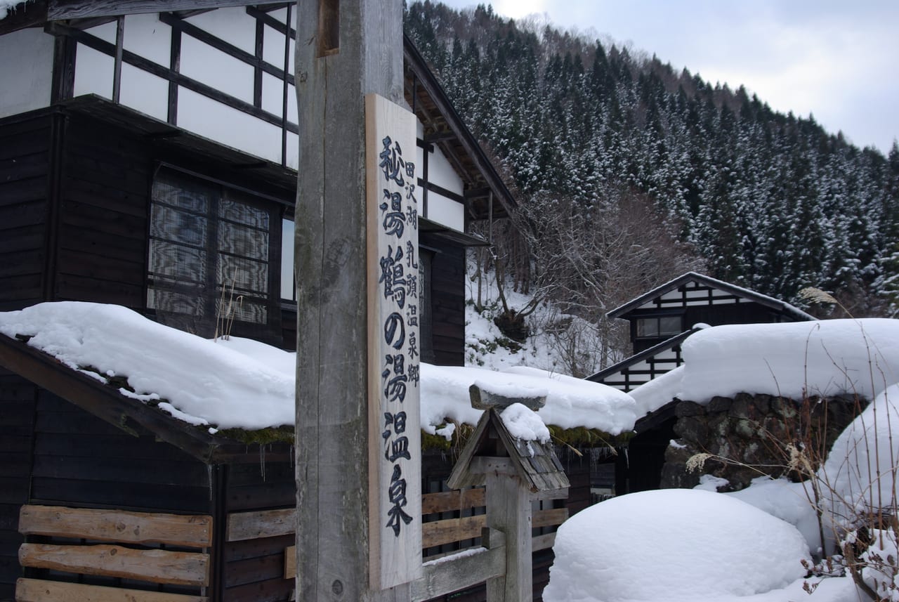 Snow-covered wooden buildings of Tsuru-no-yu at Nyuto Onsen with a signboard reading Hito Tsuru-no-yu Onsen