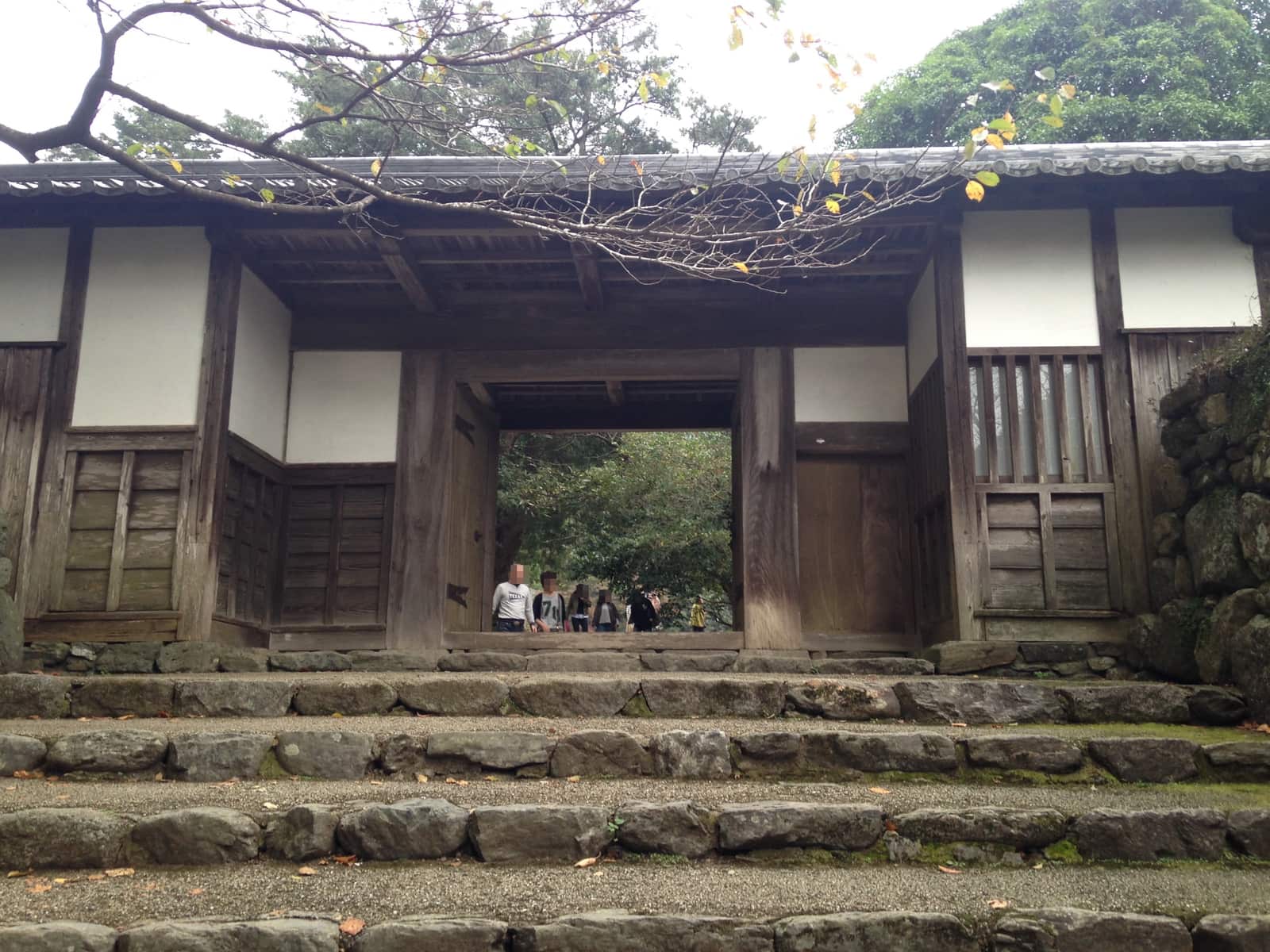 The timber facade and white plaster of the Nagayamon gate at Akizuki Castle ruins, stone steps and shade in front