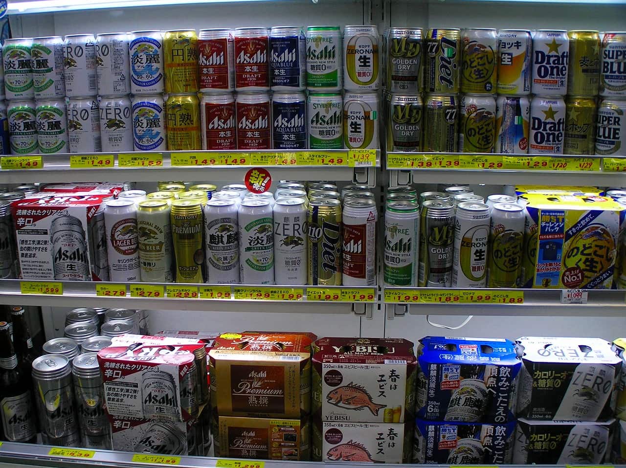 Three shelves of a Japanese discount store beer aisle: rows of 350 ml aluminium cans including Kirin Tanrei, Asahi Honnama, Style Free, Sapporo Draft One and Nodogoshi Nama, each slot fronted by a yellow handwritten price tag ranging from 120 to 299 yen, with six-can cartons on the bottom shelf