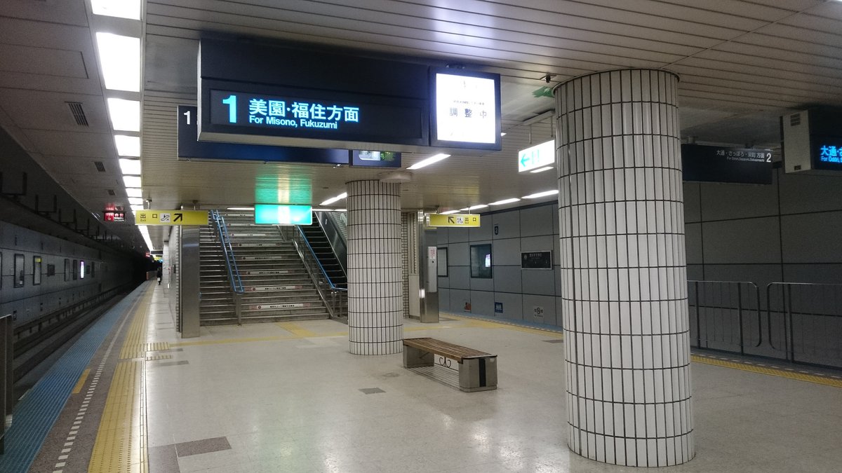 豊水すすきの站的地下月台，天花板吊著的電子指示牌寫著「1 美園・福住方面 For Misono, Fukuzumi」，月台中間有白色磁磚圓柱、一張木長椅和往出口的樓梯，月台上沒有人