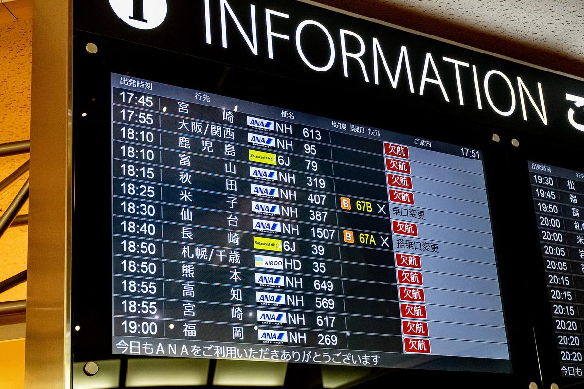 Close-up of a Japanese domestic departure board where several flights show cancelled and schedule-changed statuses beside marker symbols