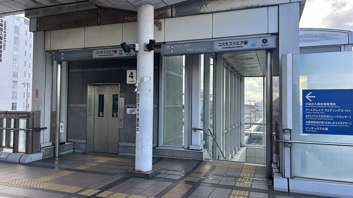 コスモスクエア站 4 號出入口:灰色站名招牌「コスモスクエア駅 4 出入口」,左邊是電梯、右邊是往下的樓梯;右側藍色指標牌箭頭朝左,列出大阪出入国在留管理局、ATC、大阪府咲洲庁舎,最下面一行是インテックス大阪