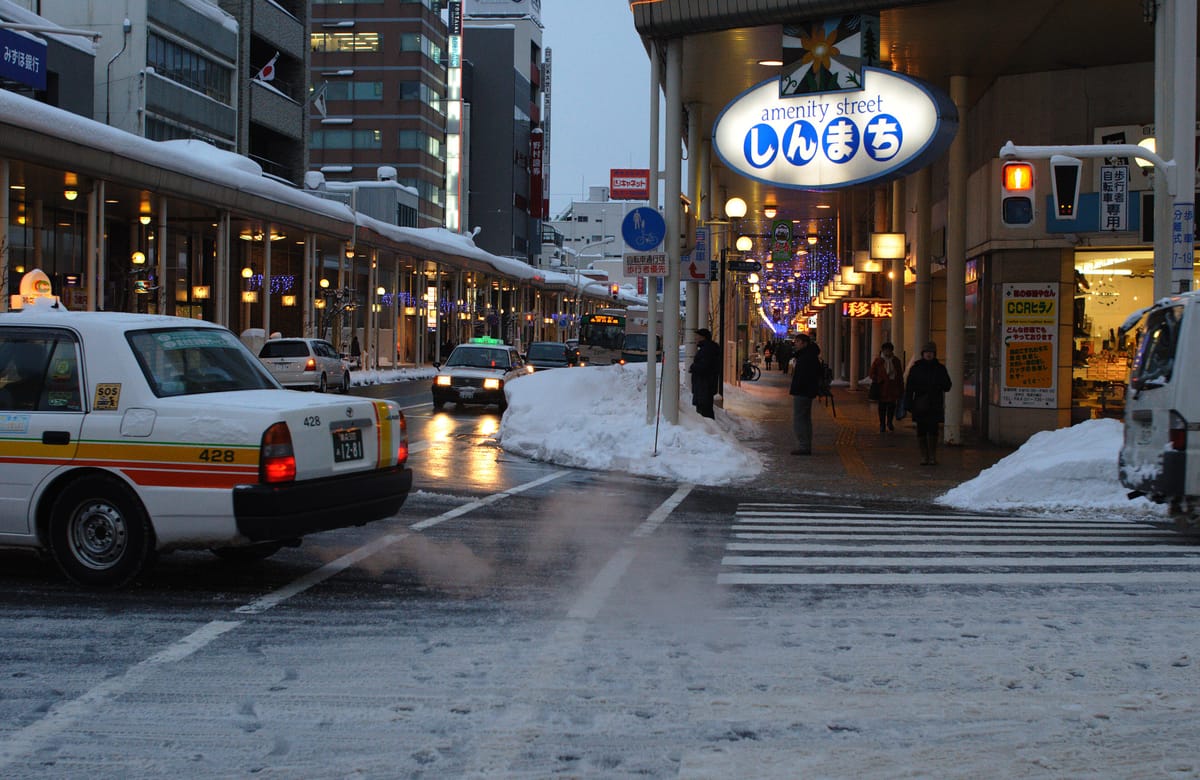 Shinmachi street in Aomori city in mid-January, the roadway under packed snow with a wall of cleared snow banked between pavement and traffic lane