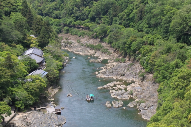 A wooden Hozugawa boat shooting through rapids with a boatman poling at the back