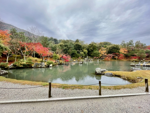 Tenryuji's Sogen-chi pond garden with the Arashiyama mountain ridge reflected in the still water and red maple trees in the foreground