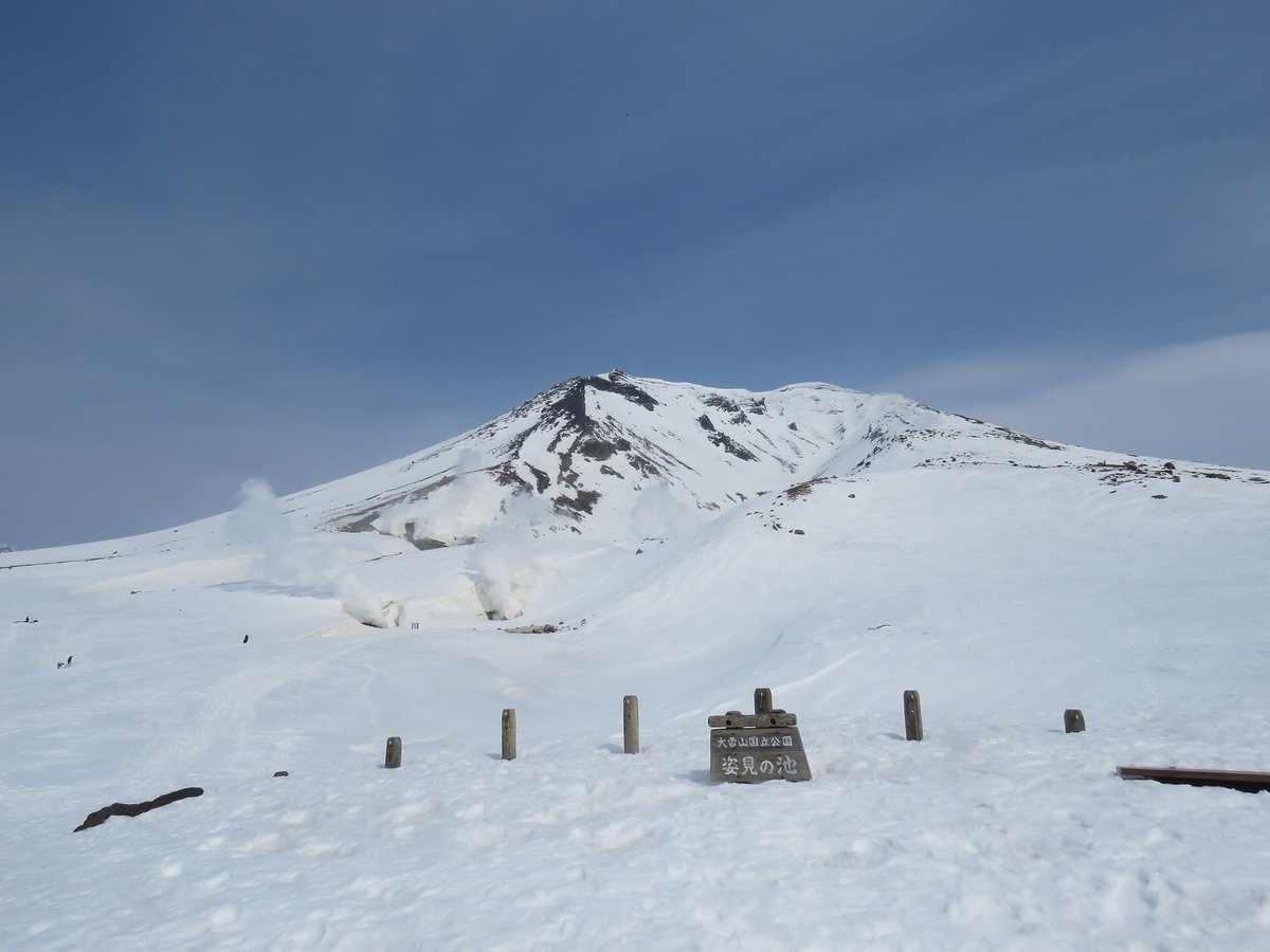 雪原上露出一排木樁和一塊木牌,牌上寫著「大雪山国立公園 姿見の池」,池子和步道完全被雪蓋住,後方是冒著噴氣的旭岳