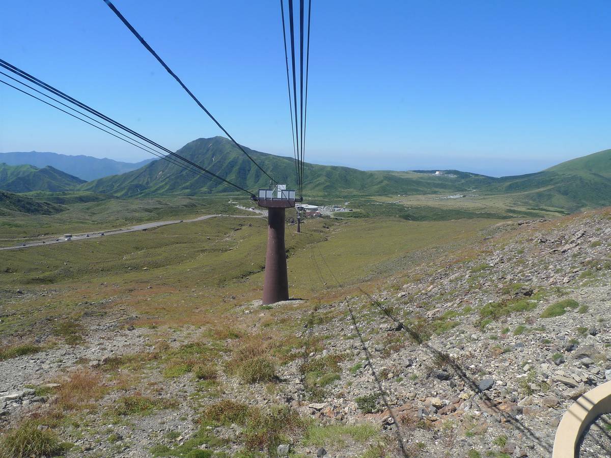 Mount Aso Ropeway gondola in service above the grassland, Mount Eboshi in the background