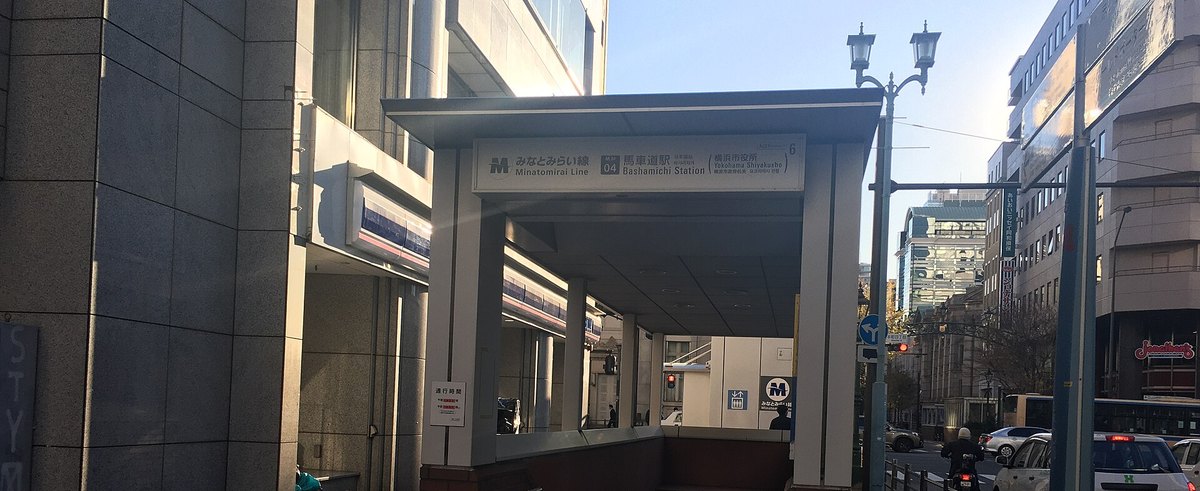 馬車道站 6 號出口的地面出入口：灰白色頂棚下掛著「みなとみらい線 馬車道駅 Bashamichi Station（横浜市役所）」的站名牌，牌子右上角標著數字 6；左邊緊鄰一間便利商店，右邊是立著古典造型路燈的馬路