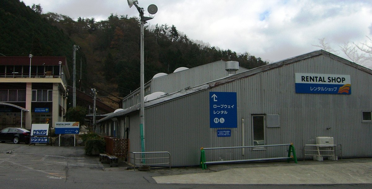 2008 年 12 月的琵琶湖 Valley 山麓：右側灰色鐵皮建築的牆上掛著 RENTAL SHOP レンタルショップ 招牌，以及指向纜車與租借的藍色箭頭牌；左側米色建築掛著纜車乘車處的藍牌；後方是落葉的山坡，地上沒有積雪