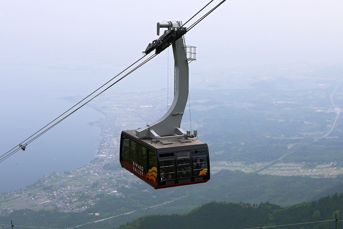 2010 年 5 月琵琶湖 Valley 的纜車車廂：黑色車身、下緣紅色，側面寫著 BIWAKO VALLEY，懸在兩條鋼索下，背景是霧中的琵琶湖湖岸與田地