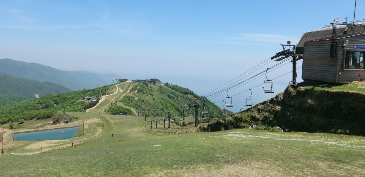 2014 年 6 月沒有雪的琵琶湖 Valley 山頂：前景是草坡，中間小山頭上有一排建築，吊椅的纜線從右側的木造小屋往山谷延伸，左下有一座藍色蓄水池，右後方是霧白的琵琶湖