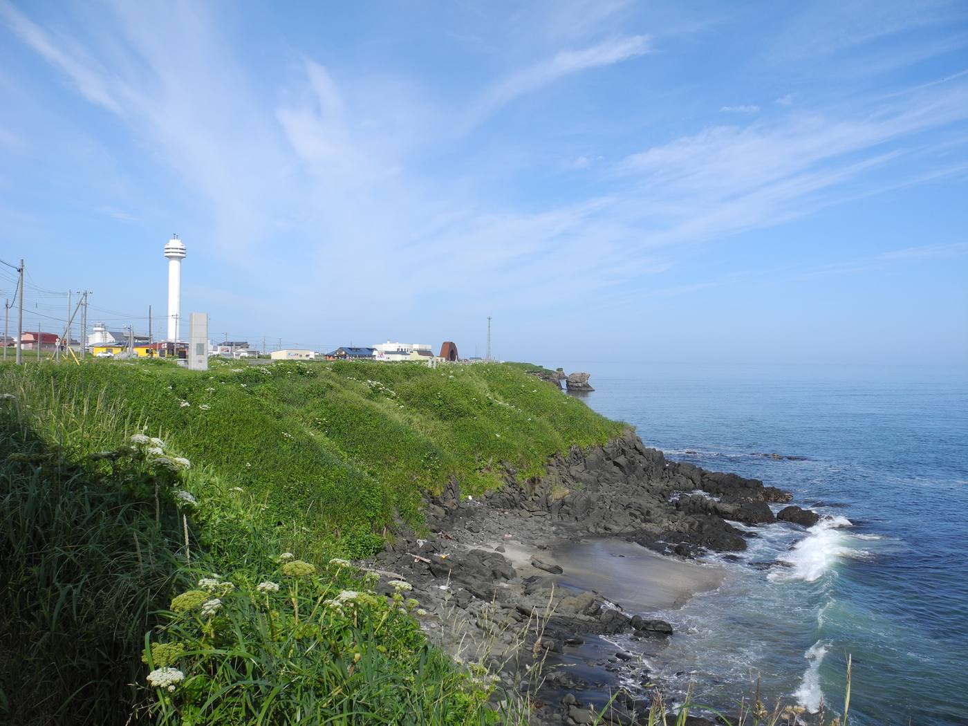 The grassy headland and white lighthouse of Cape Nosappu above the rocky Pacific shoreline