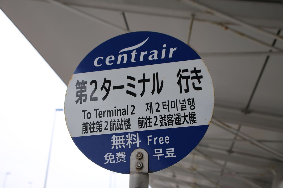 接駁車站牌特寫:藍白圓牌上方是 centrair 標誌,中間寫「第2ターミナル 行き」,下面有英文 To Terminal 2、韓文與簡繁中文「前往第2航站楼」「前往2號客運大樓」,最下面寫「無料 Free 免费 무료」