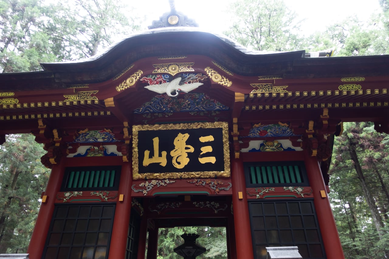 三峯神社隨身門，朱紅與彩繪雕刻的山門被高大杉林環抱