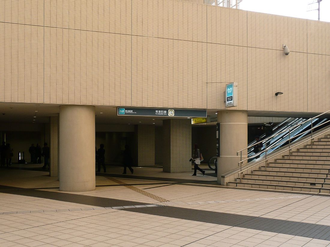 米色磁磚大樓底下的東京 Metro 東池袋站出入口，橫樑上掛著深綠色「東池袋駅 有楽町線 Y10」站名牌，右側是手扶梯與樓梯，前面是空曠的磁磚廣場